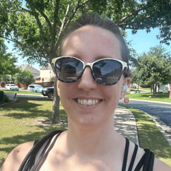 A photo of a smiling woman with her hair up, fun gold and black sunglasses, and a nose piercing.