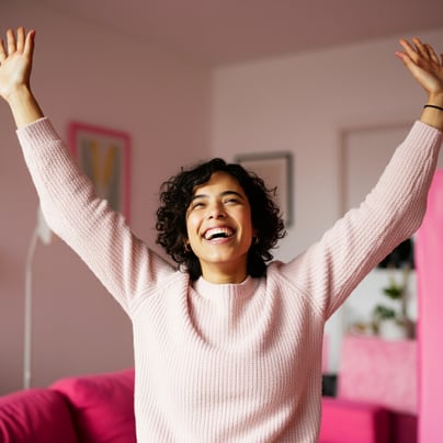 happy, energetic, and stress-free woman at home with her hands in the air. 